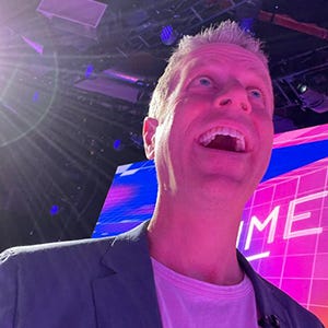 Geoff Keighley looks joyously off the corner of the screen while bathed in pink light