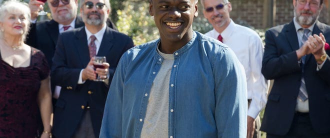 Still image from Get Out. Daniel Kaluuya smiling amongst but separate from partygoers.
