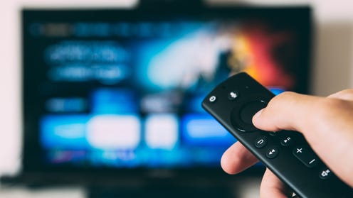 Photo of a hand holding up a remote at a blurry tv