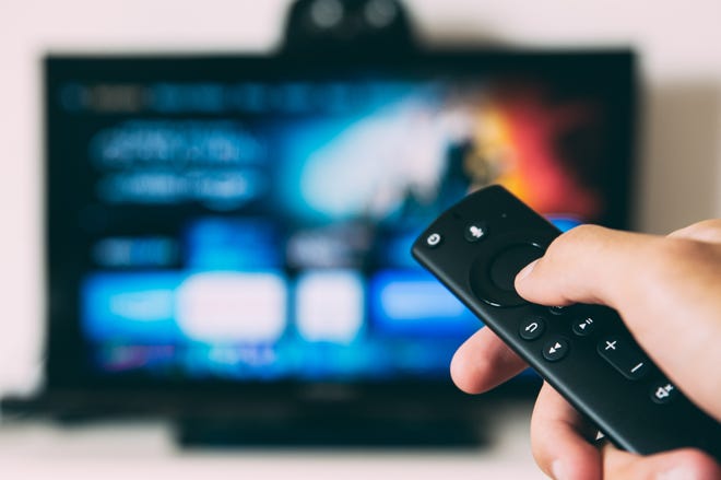 Photo of a hand holding up a remote at a blurry tv