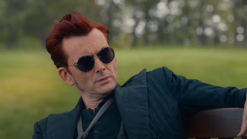 Still image of David Tennant as Crowley sitting outside on a bench