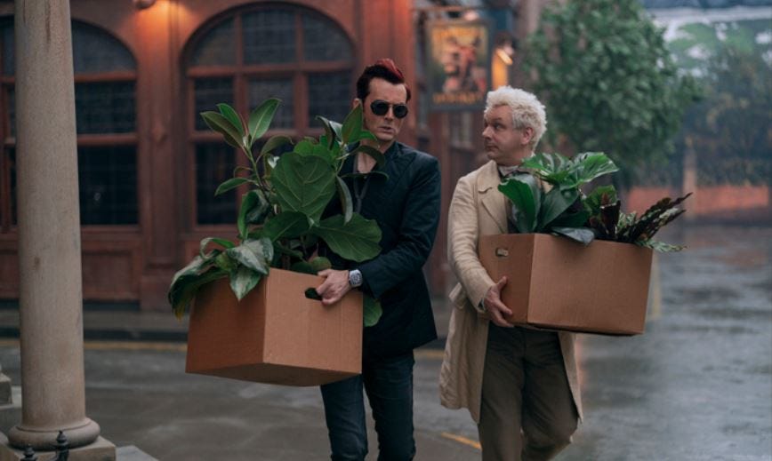 Crowley and Aziraphale walking down the street carrying boxes of Crowley's plants