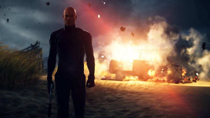 A screenshot of Agent 47 (Ian Hitman) walking away from an exploding truck on a beach, looking all cool