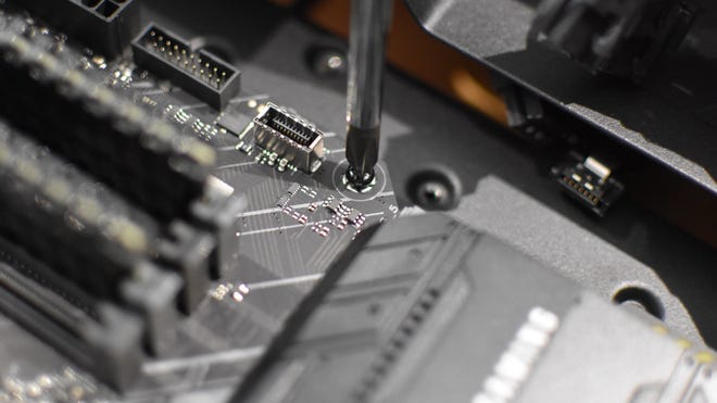 A close up of a screwdriver tightening a motherboard fitting screw.