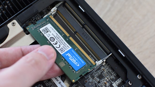 A stick of SO-DIMM RAM is lined up with the memory slots inside a mini-PC.
