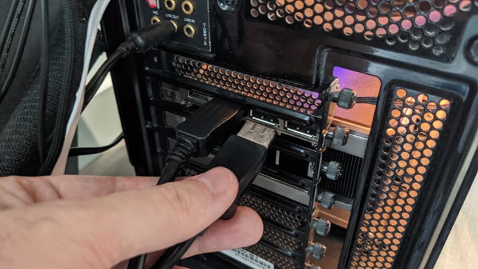 A hand plugs a DisplayPort cable into one of the display output ports on a PC's graphics card.