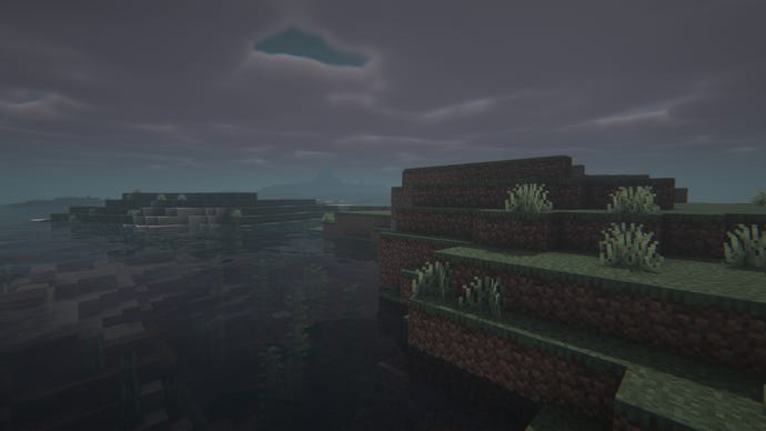 Close-up of some grass next to a river in a foggy Minecraft landscape.