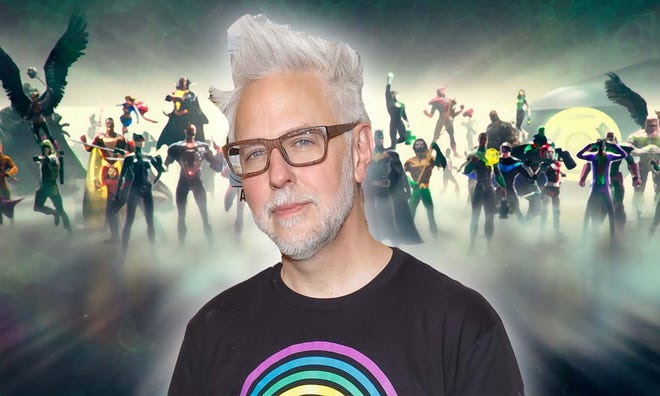 Image featuring James Gunn wearing glasses and a black tshirt with DC heroes in the background