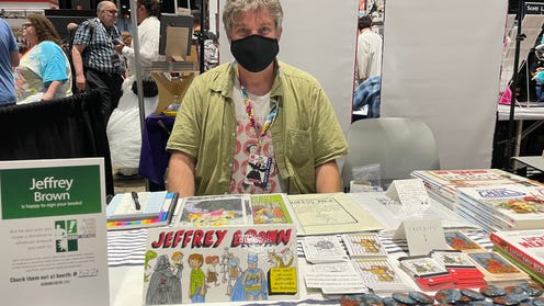 Photograph of Jeffrey Brown wearing a mask sitting behind his table at C2E2