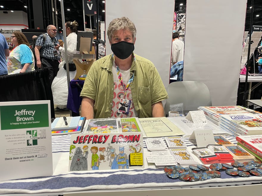 Photograph of Jeffrey Brown wearing a mask sitting behind his table at C2E2