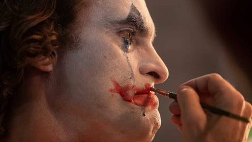 Image of Joaquin Phoenix as the Joker putting on clown makeup