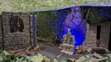 A photograph of the stage-like playing area for Life-Size DND. We, as the viewer, peer over a vine-dense wall to see a great sword in a stone before us, some crumbling walls, and a large cut-out of an owlbear. The roof of the playing area is a vine-like mesh, and the floor is taped into a grid.