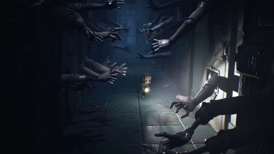 Mono from Little Nightmares II, a small boy with a brown paper bag on his head, runs down a corridor holding a torch. Tens of wooden dummy hands are reaching for him from behind locked metal doors
