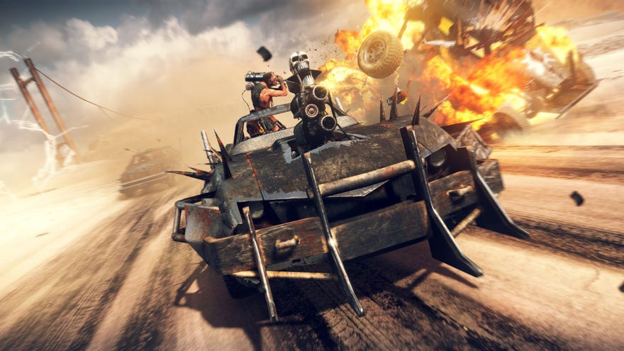 A screenshot of the game Mad Max, where Max drives his souped up yet rusty car towards the camera, explosions in the background