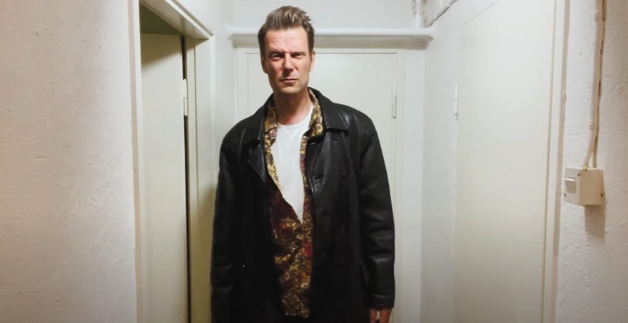 A still of a video showing Sam Lake in his Max Payne clothes.