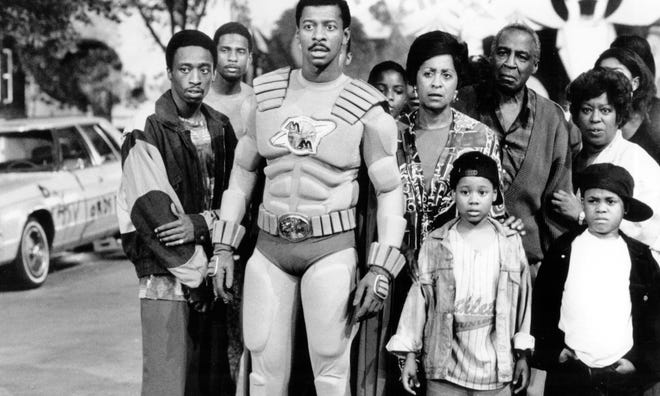 A black and white photo of a group of people, with a man wearing a superhero costume in the middle
