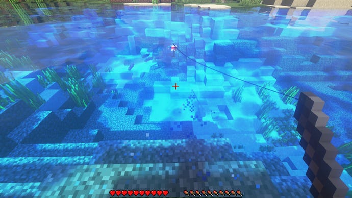 A player in Minecraft fishes in a lake. Between the bobber and the player, a v-shaped set of particles indicates the presence of a fish.