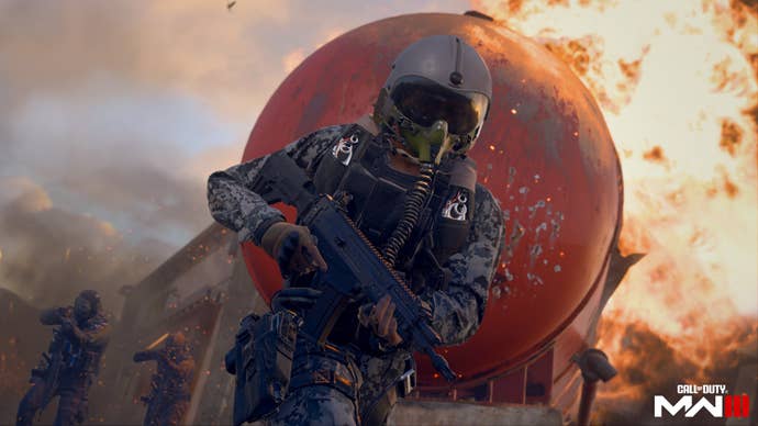 Un soldado en Modern Warfare 3 está de pie, con el arma en alto por encima de su cintura, en una pose de acción.  Detrás de él, llamas y un cielo polvoriento.