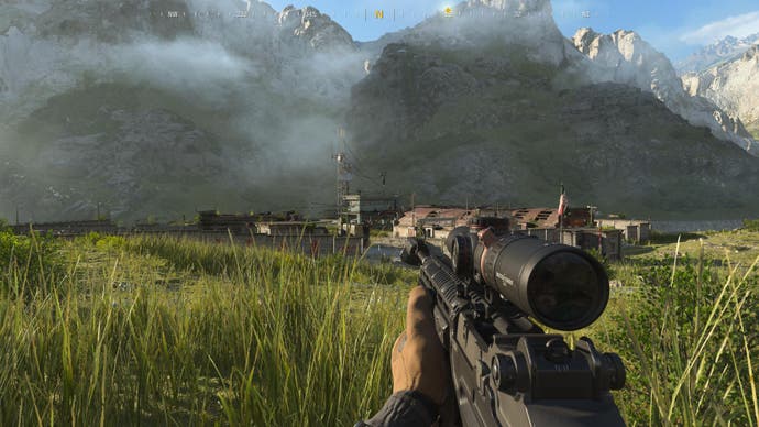 modern warfare 3 screenshot of the player holding a sniper rifle, in a grassy field overlooking an outpost with vast mountains in the background