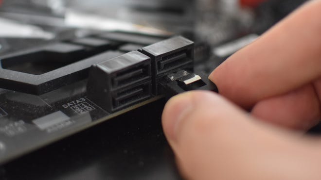 A SATA cable being connected by hand to a motherboard's SATA port.