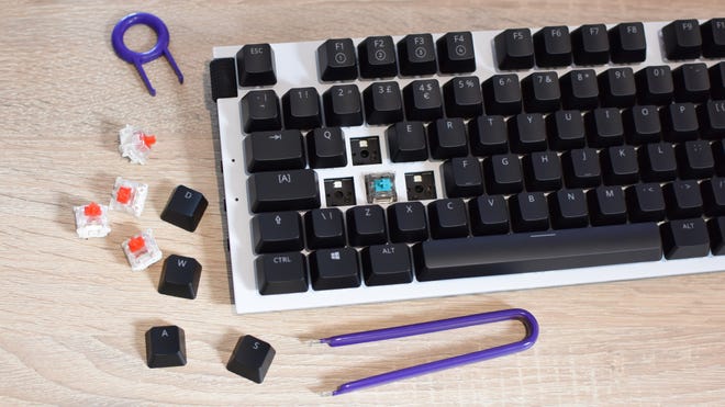 Un clavier de jeu NZXT Function en cours de remplacement à chaud de ses commutateurs à clé WASD.  Plusieurs touches et commutateurs supprimés se trouvent à côté du clavier, à côté de certains outils.