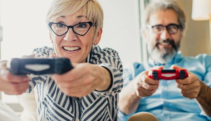 A 50+ woman and a 50+ man play games holding PS4 controllers