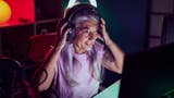 A woman with long grey hair pulls on a gaming headset in front of a glowing screen.