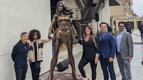 Five people standing next to Wonder Woman statue