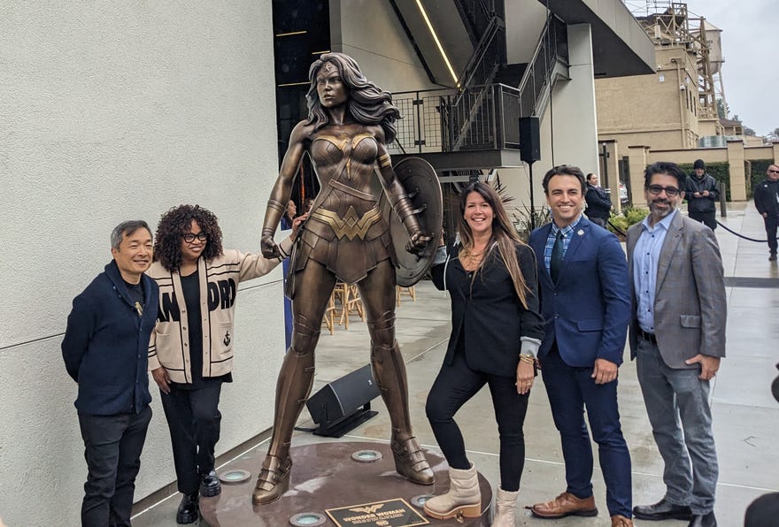 Five people standing next to Wonder Woman statue