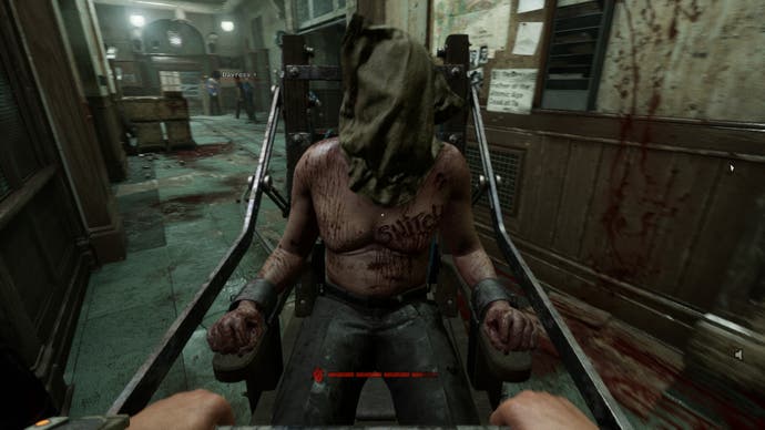 A screenshot from an Outlast Trails review showing a man strapped to a metal cart with a bag over his head, 
