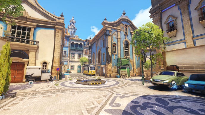 An establishing shot of Esperanca Portugal, a map in Overwatch 2, showing a town square area with cars parked on the right hand side.