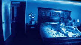Paranormal Activity poster showing a woman and a man in bed being recorded, the woman pointing at a shadow at their open door.