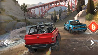 Screenshot of Rebel Racing showing a red off-road truck racing through a canyon with a bridge overhead, with a blue truck slightly ahead of it