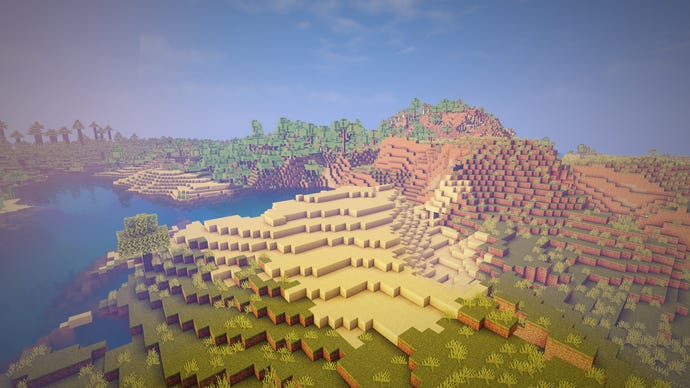 A bird's eye view of a Minecraft landscape, with sand in the foreground, forest in the background, and a lake on the left-hand side.