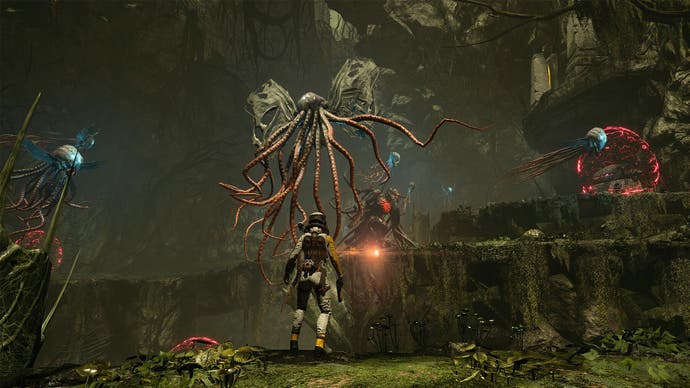 Captura de pantalla de Returnal, que muestra a la protagonista Selene parada frente a una forma de vida alienígena parecida a un pulpo.