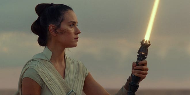 Daisy Ridley as Rey looking at her yellow lightsaber