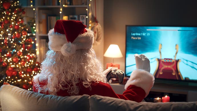 A photo looking in at a Christmas gaming scenario in a house, only, it's Santa Claus we see the back of who is gaming on the TV. And they're playing a sleigh-racing game. A Christmas tree shines brightly beside them.