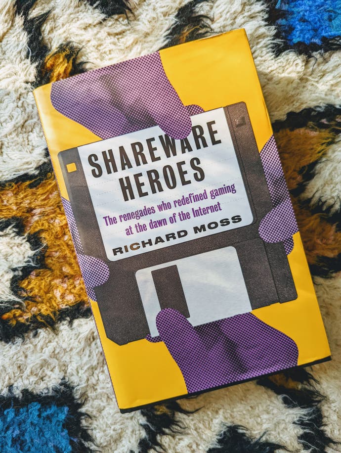 The Shareware Heroes book, pictured on Bertie's wonderful multi-coloured rug. The book cover has four purple hands pulling at a floppy disk bearing the name of the book and the author Richard Ross. The rest of the book is coloured yellow.
