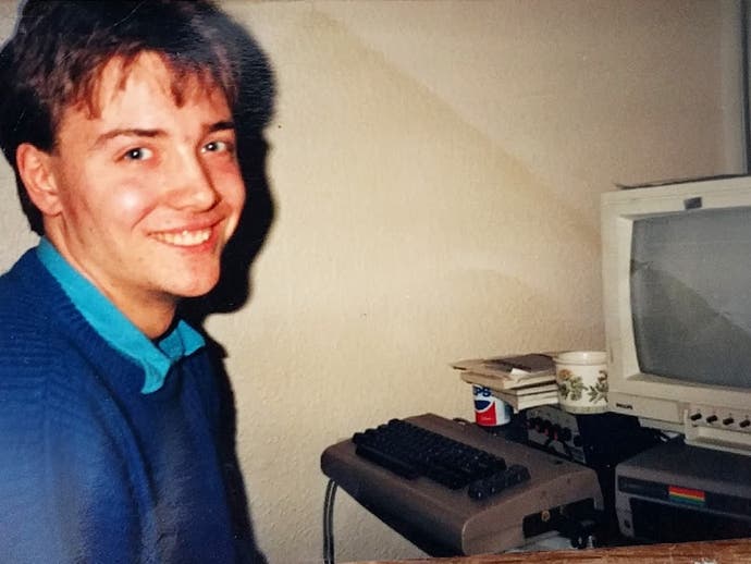 عکسی از یک سایمون پیک جوان با کمودور 64 خود. پیک لبخندی برنده، رو به دستگاه می‌تابد.