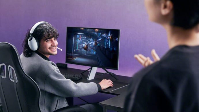 Promo image of Sony's Inzone headset and monitor, showing someone sat at a desk playing a game on said monitor, while wearing said headset, looking to someone in the forground, smiling.