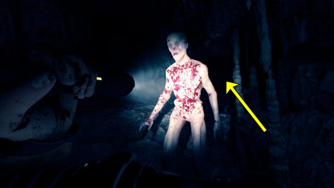 The player in Sons Of The Forest shines their flashlight on a bloodied Cave Cannibal enemy in a cave.