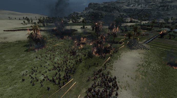 A pitched battle in Total War: Pharaoh with infantry meeting on a plain, and palm trees and grasses burning