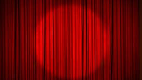A red stage curtain, drawn, with a circular spotlight shining on the middle of it.