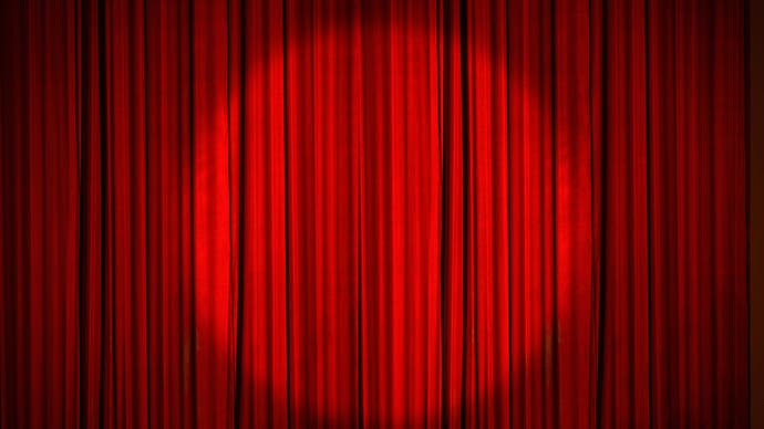 A red stage curtain, drawn, with a circular spotlight shining on the middle of it.