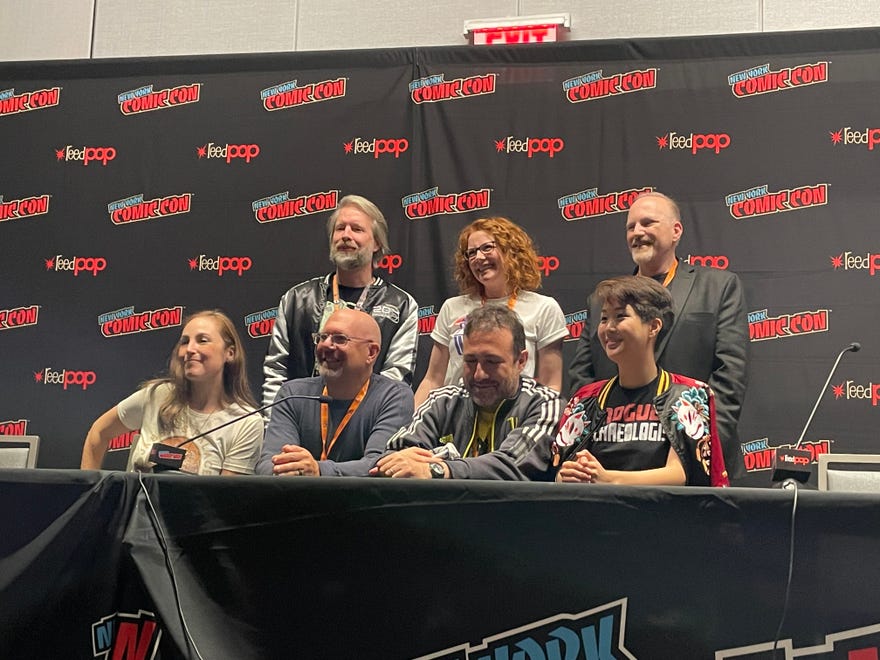 Photograph of seven panelist smiling towards a camera with the reedpop/nycc banner behind them