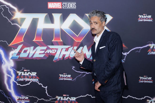 Taika Waititi posing in front of Thor Love and Thunder background
