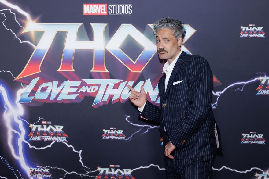 Taika Waititi posing in front of Thor Love and Thunder background
