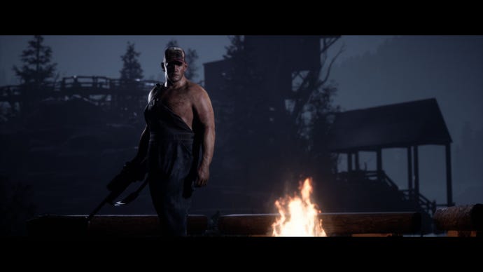 A large menacing man holding a rifle and wearing dungaree overalls (hanging off one shoulder) stands by the campfire in The Quarry