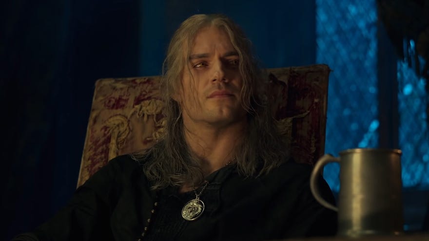 Netflix's The Witcher series season 2 - Geralt sits in an upholstered chair at night in kaer morhen next to a mug, wearing his Witcher medallion.