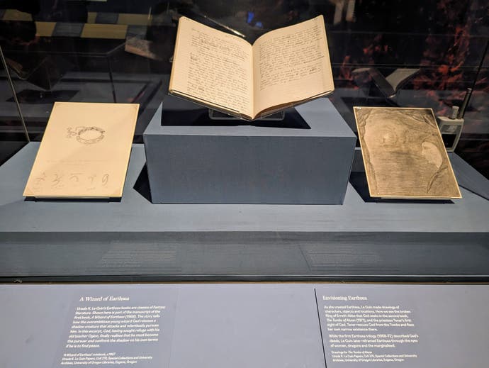 A photograph showing a notebook and two pencil sketched pictures in an exhibition. These are made by Ursula le Guin, the legendary sci-fi and fantasy author, and helped her shape her Earthsea stories.
